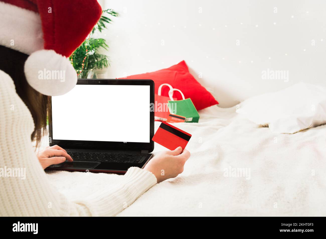 Faceless woman in santa hat lying on bed at home with laptop and plastic card Stock Photo