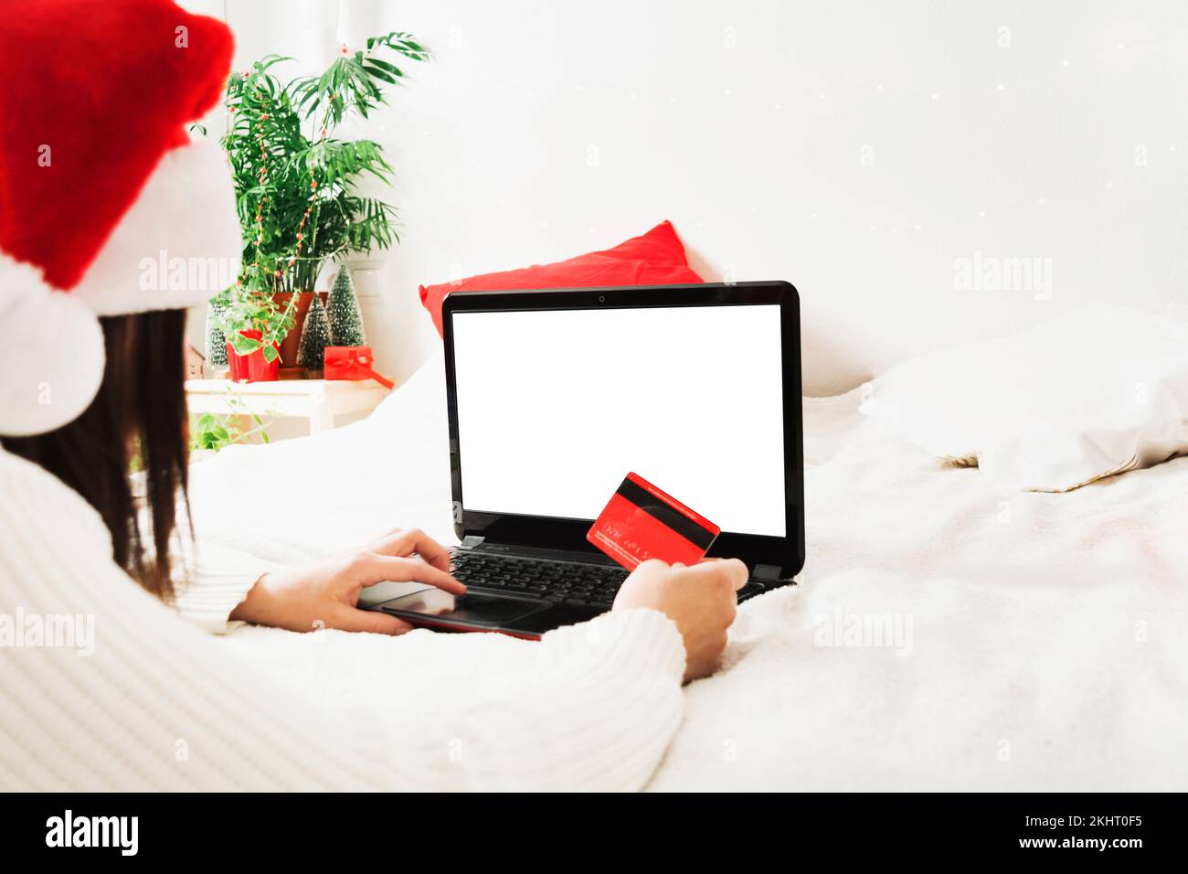 Faceless woman in santa hat lying on bed at home with laptop and plastic card Stock Photo