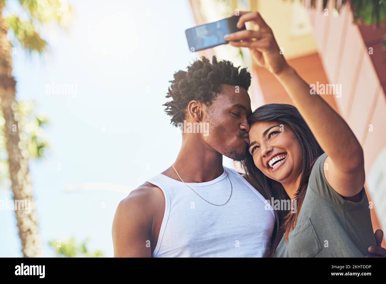 Selfie, kiss and interracial couple with phone in the city, date and happiness with memory together. 5g technology, love and black man and woman with Stock Photo