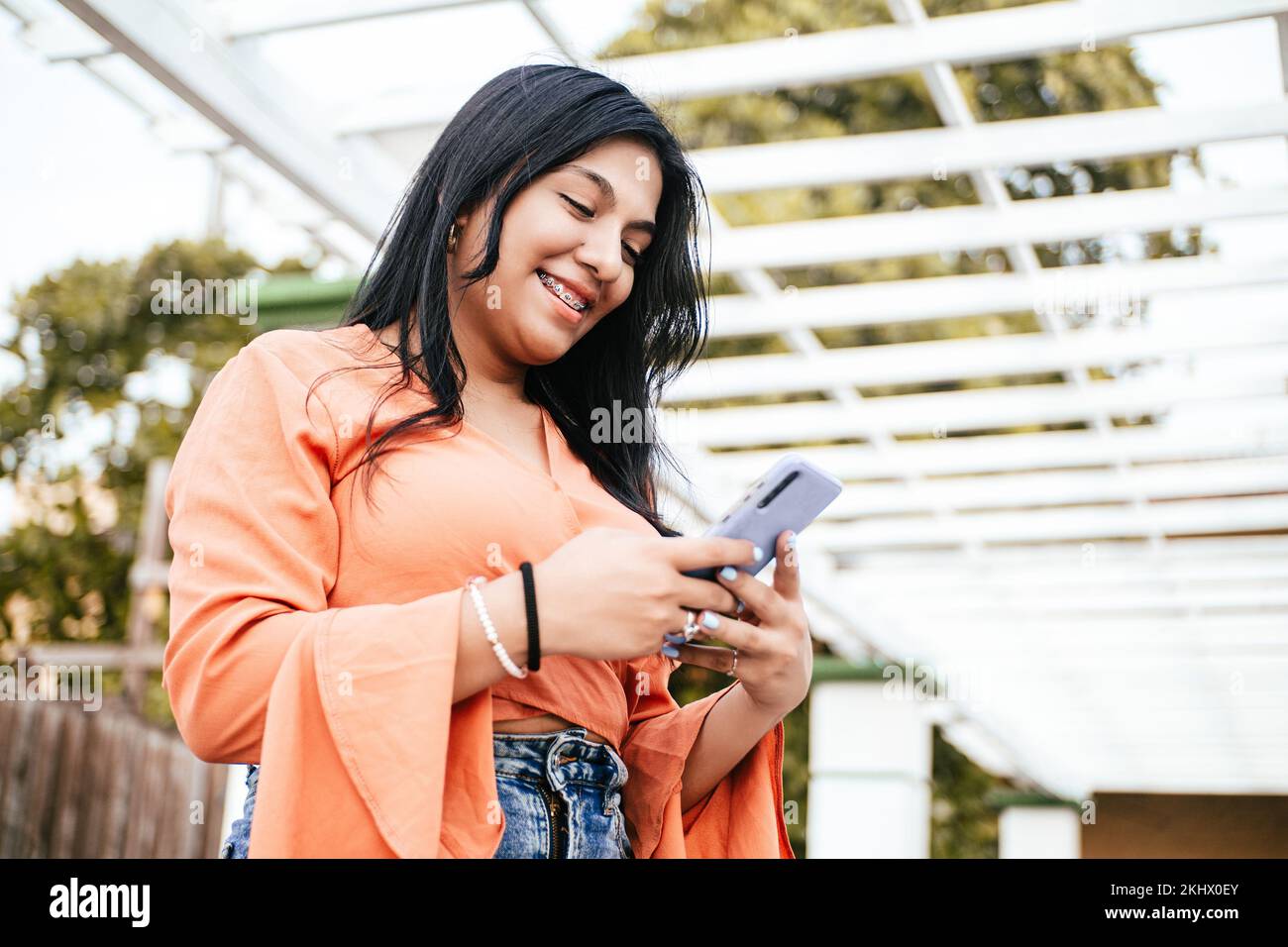 A smiling Latin female using a mobile phone outdoors Stock Photo