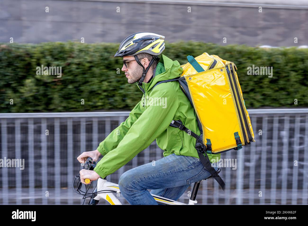 Fast delivery man riding in the city, young courier dressed in technical and sports clothing, with helmet and backpack for food, panning effect, fast Stock Photo