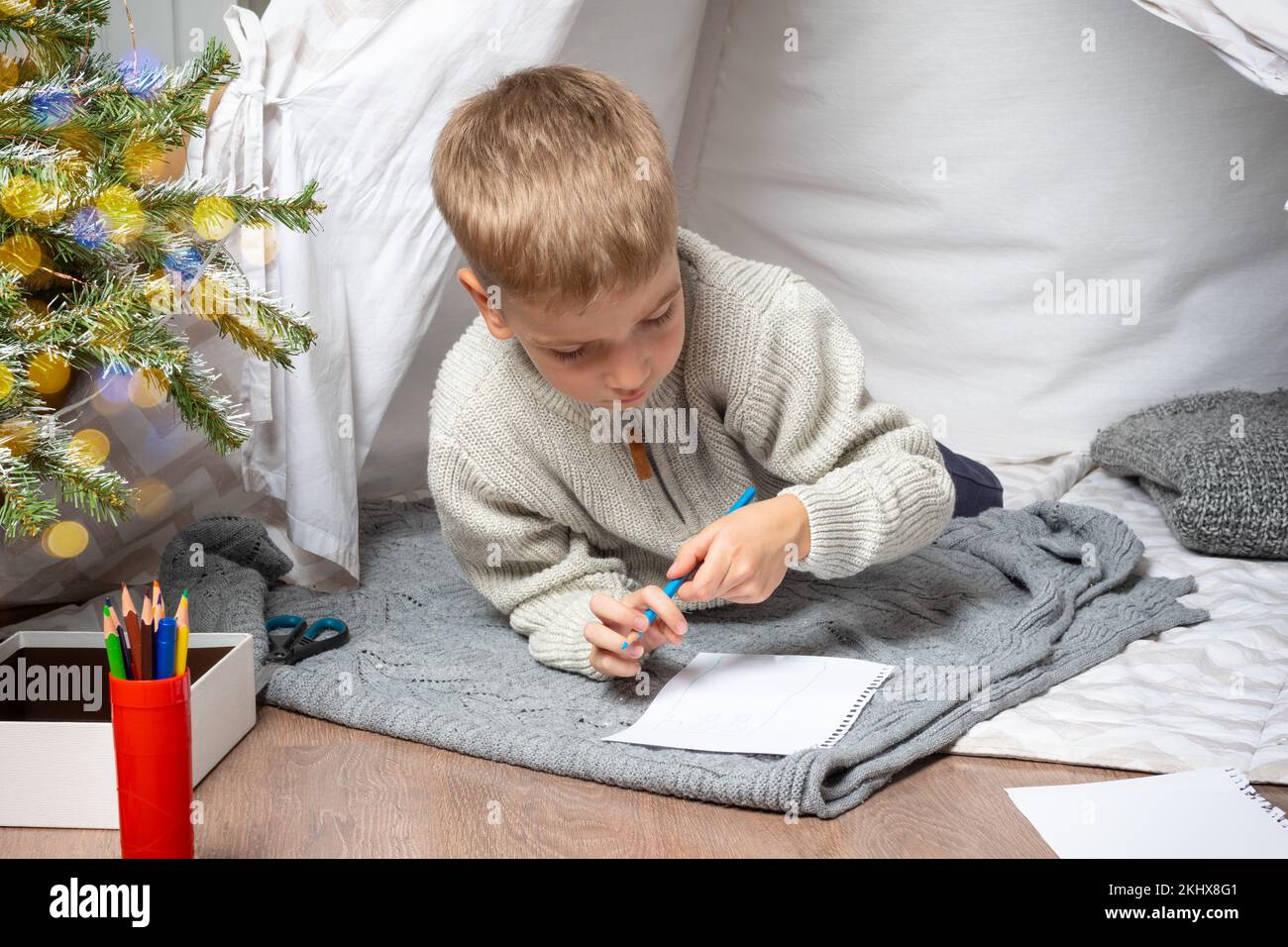 A wish list for a Christmas miracle. A little cute boy draws a dream gift from Santa Claus at home. The child hopes for a New Year's miracle Stock Photo