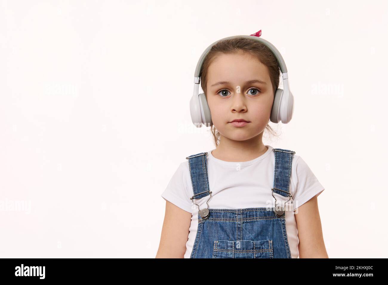 Cute baby girl wearing wireless headphones, isolated over white background with copy space for