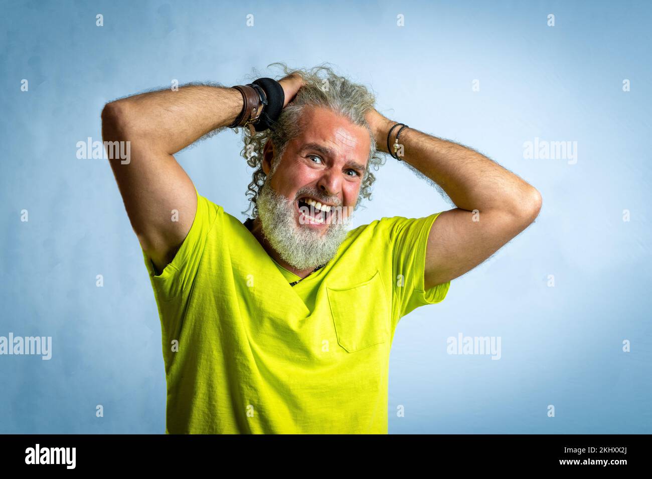 Hipster bearded man looking at the camera with worried and painful expression, adult male putting his hands in his hair to despair, studio shot with y Stock Photo