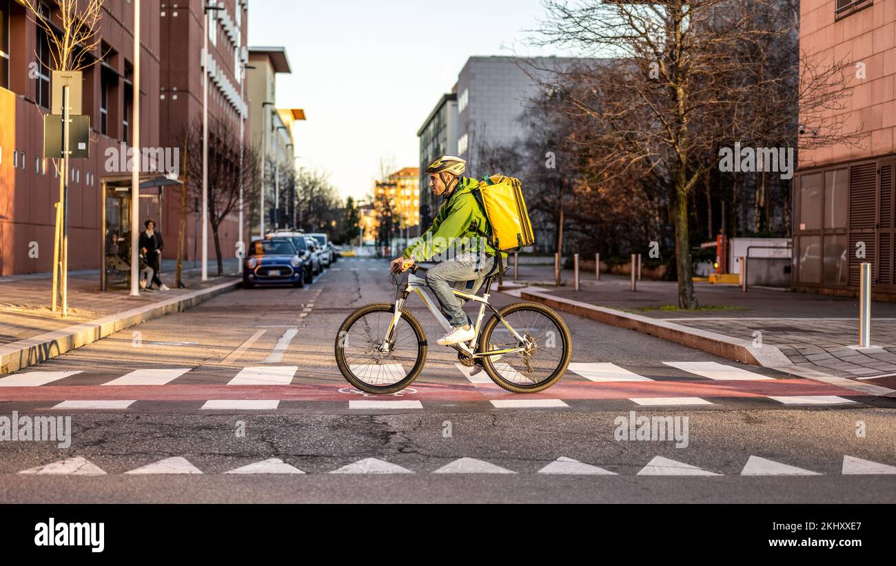 Fast and ecologic delivery service, deliveryman at work, riding city street to handing over takeaway food, boxes and dociments, black, white and yello Stock Photo