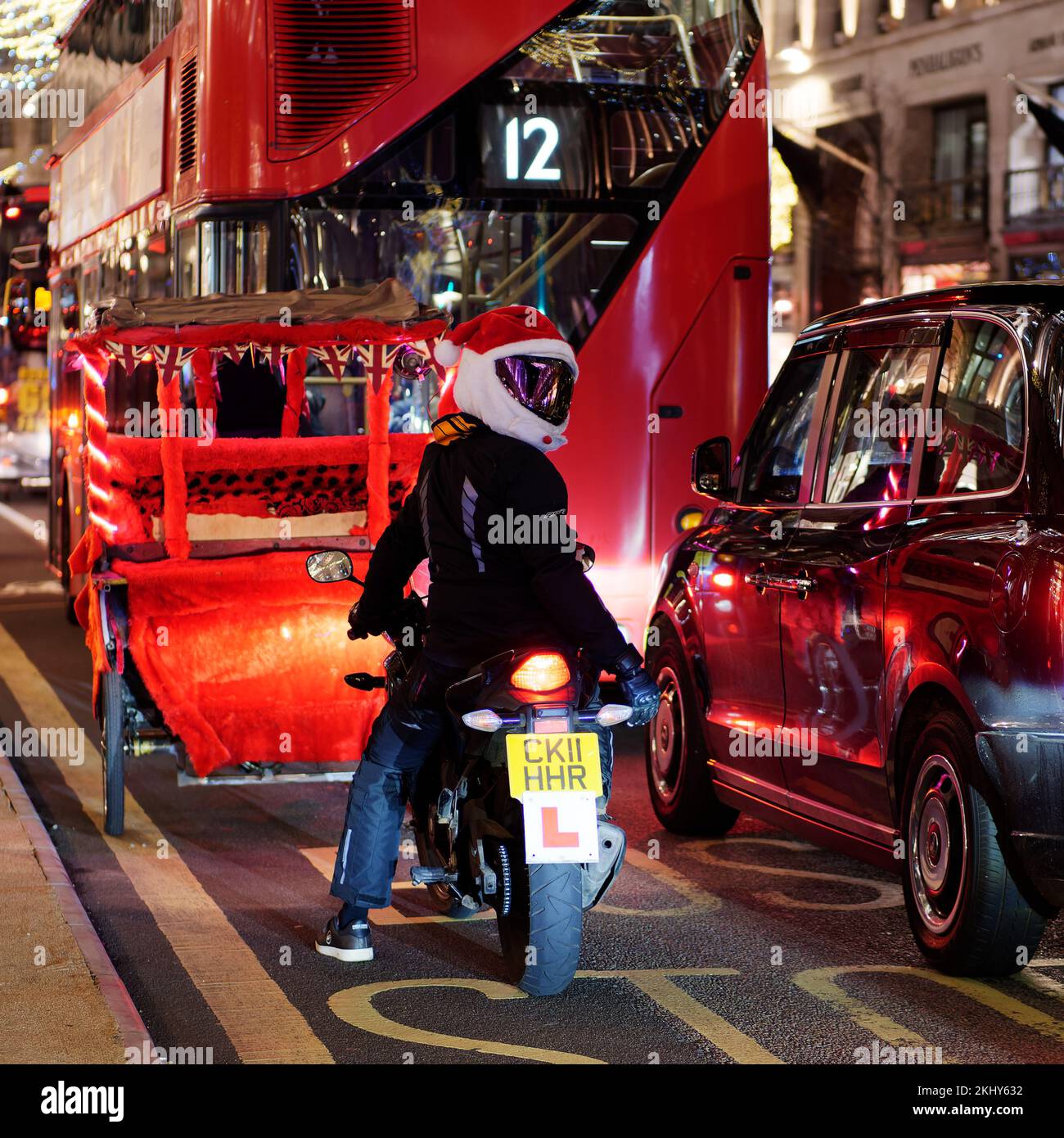 Traffic on Regent Street during the festive season with a learner motorcyclist wearing a Santa Claus hat. London. Stock Photo