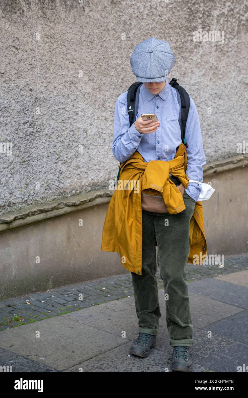 A dapper tourist, prepared for any weather, checks the directions on his phone before entering the Royal Mile from Cockburn Street in Edinburgh. Stock Photo