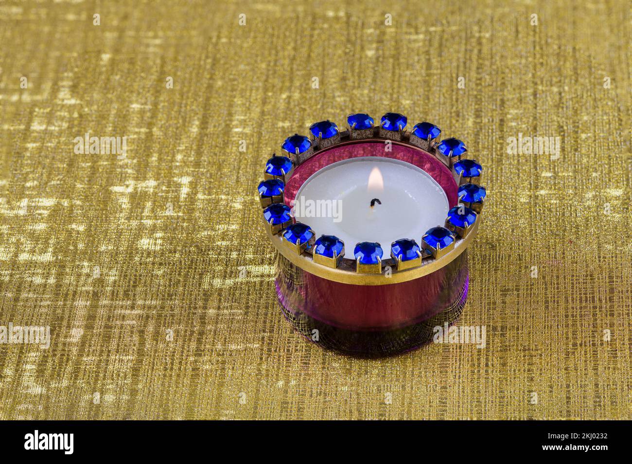 A burning tea light in a vintage purple glass holder against a golden background with texture