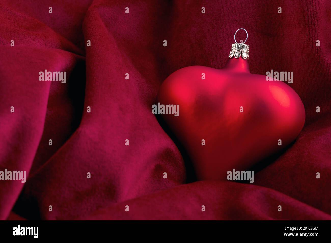 A romantic red christmas bauble in the shape of a heart on a snug and soft velvet blanket. Stock Photo