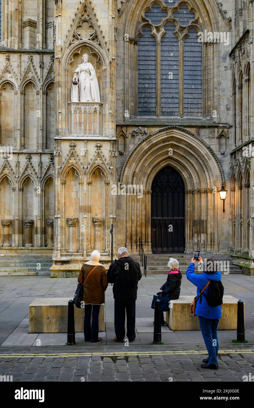 Person taking photos of new Elizabeth 2 statue on niche wearing Garter Robes (orb, sceptre) - York Minster west front, North Yorkshire, England, UK. Stock Photo