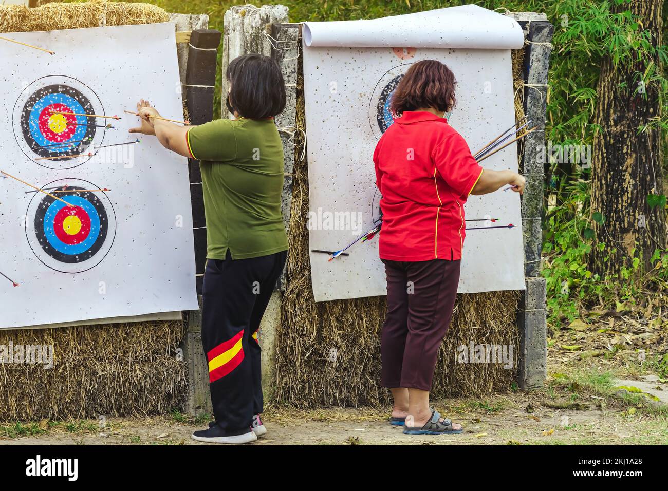 Back view of female officer wear face mask collect arrows fired from a bow on sport target. Women clearing arrows from target to start new game. Medit Stock Photo
