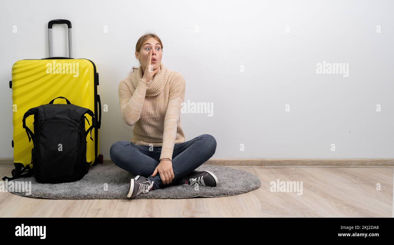 Woman traveler with suitcase in sweater ready to go to travel shouting and holding palm near opened mouth. Passenger travel abroad on weekends getaway Stock Photo