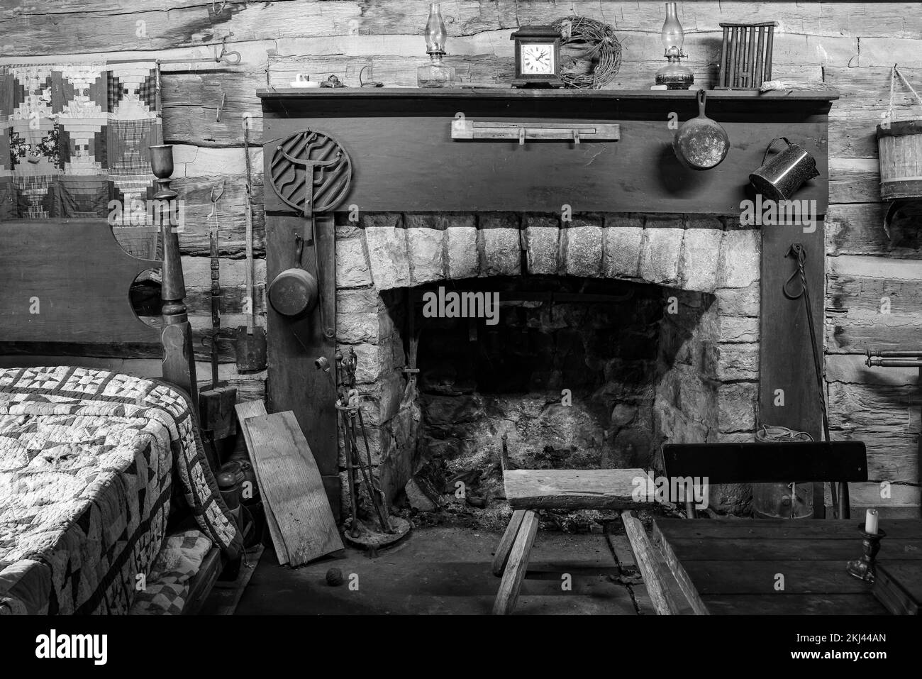 A grayscale of an old stone fireplace in a wooden cabin filled with
