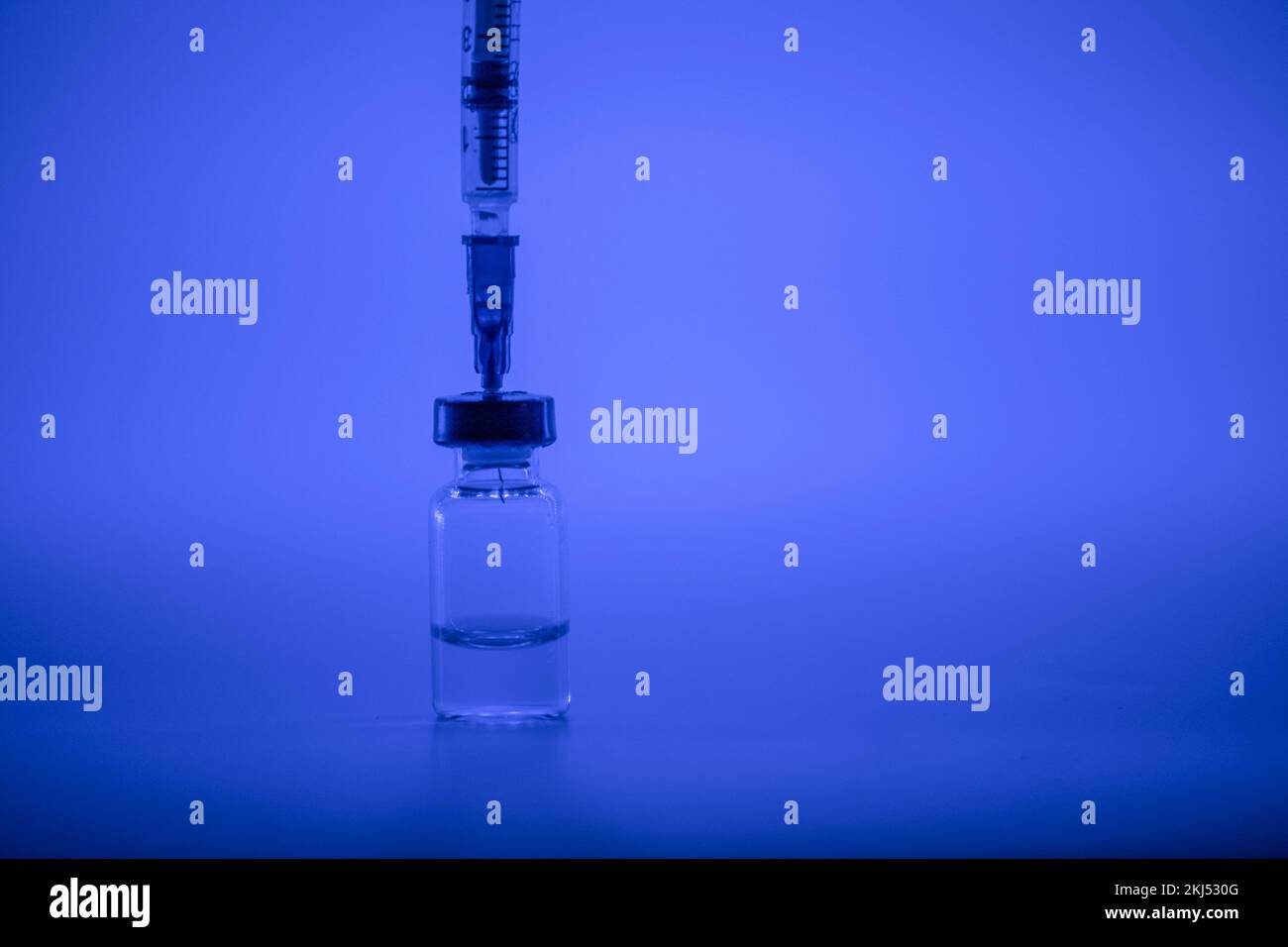 Vaccine vial, syringe with flu shot needle, vaccination medical concept, subcutaneous injection on blue background. Copy space. Test immunization and Stock Photo