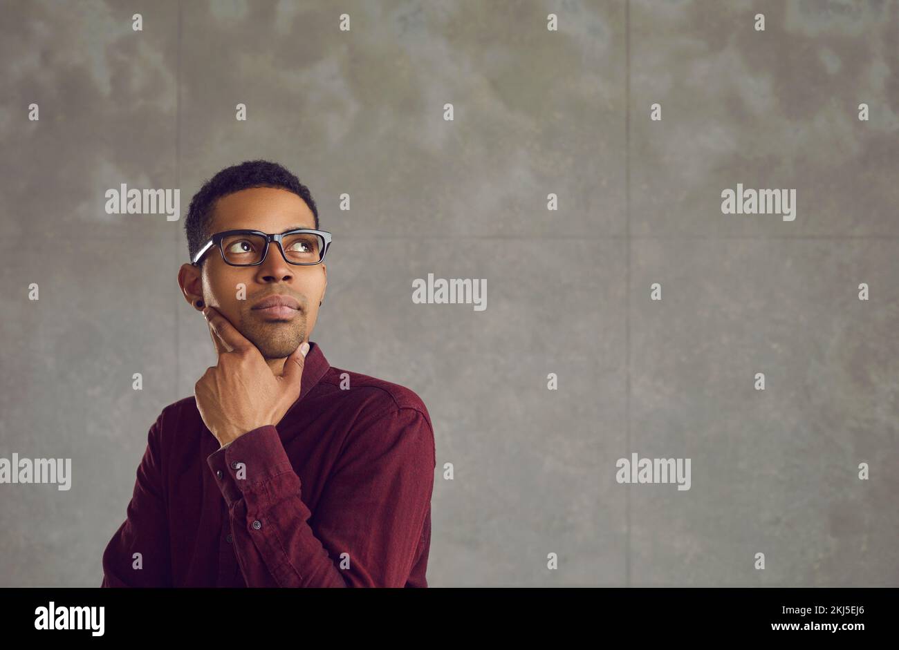 African American man with a pensive expression looks up standing on a gray concrete background. Stock Photo