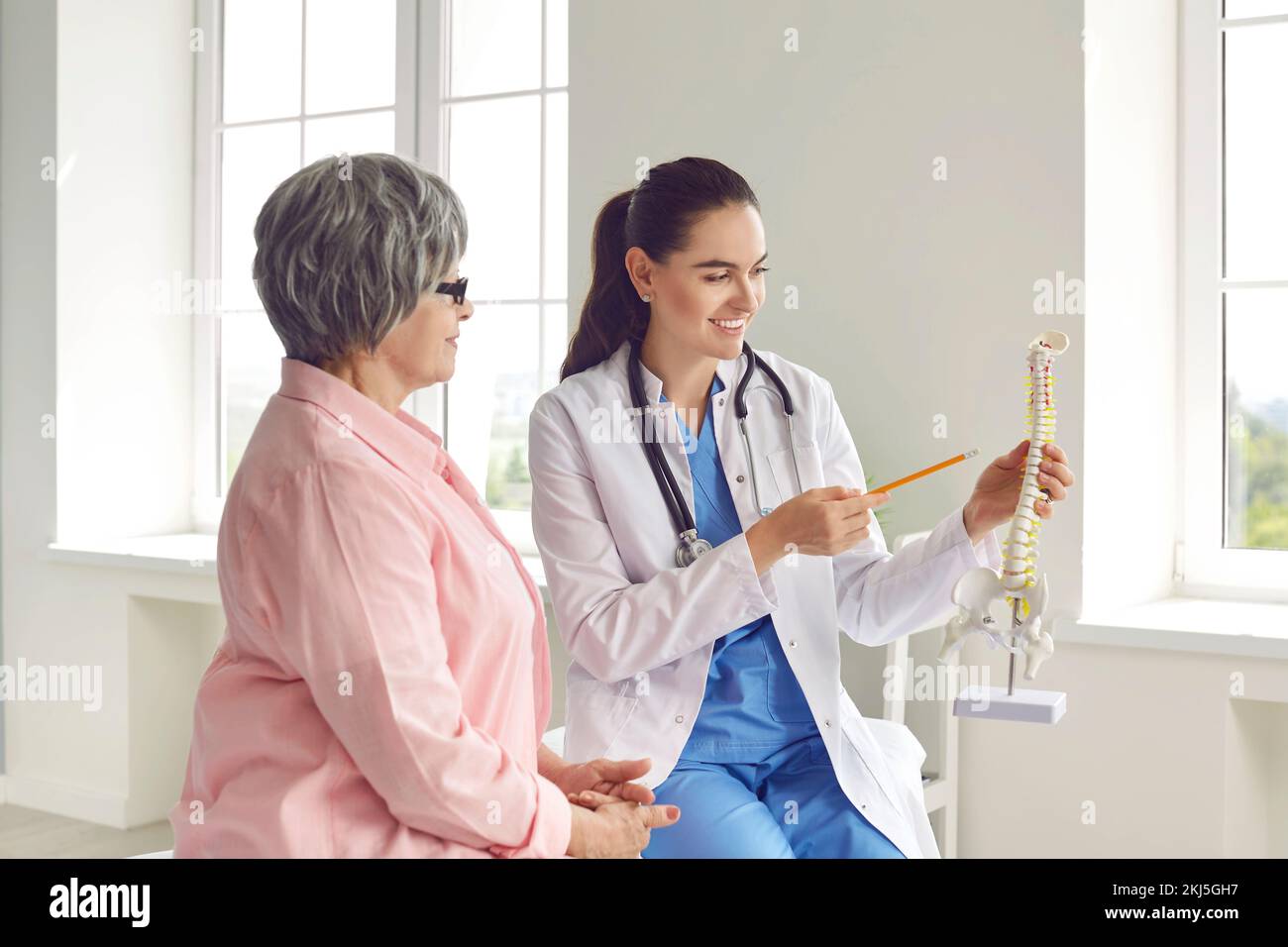 Doctor during consultation for elderly woman shows models of spine while talking about treatment. Stock Photo