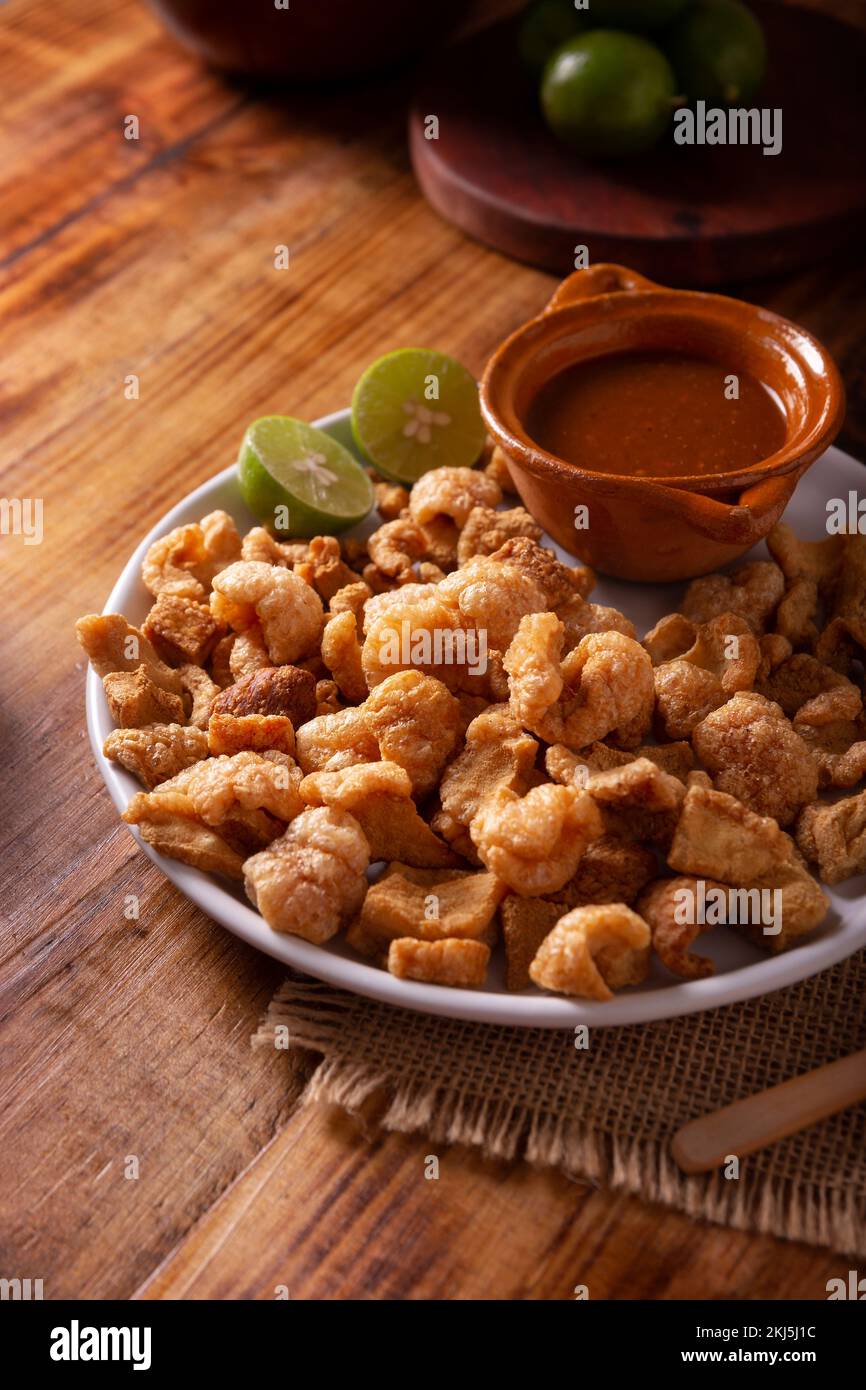 Chicharrones. Deep fried pork rinds, crispy pork skin pieces, traditional mexican ingredient or snack served with lemon juice and red hot chili sauce. Stock Photo