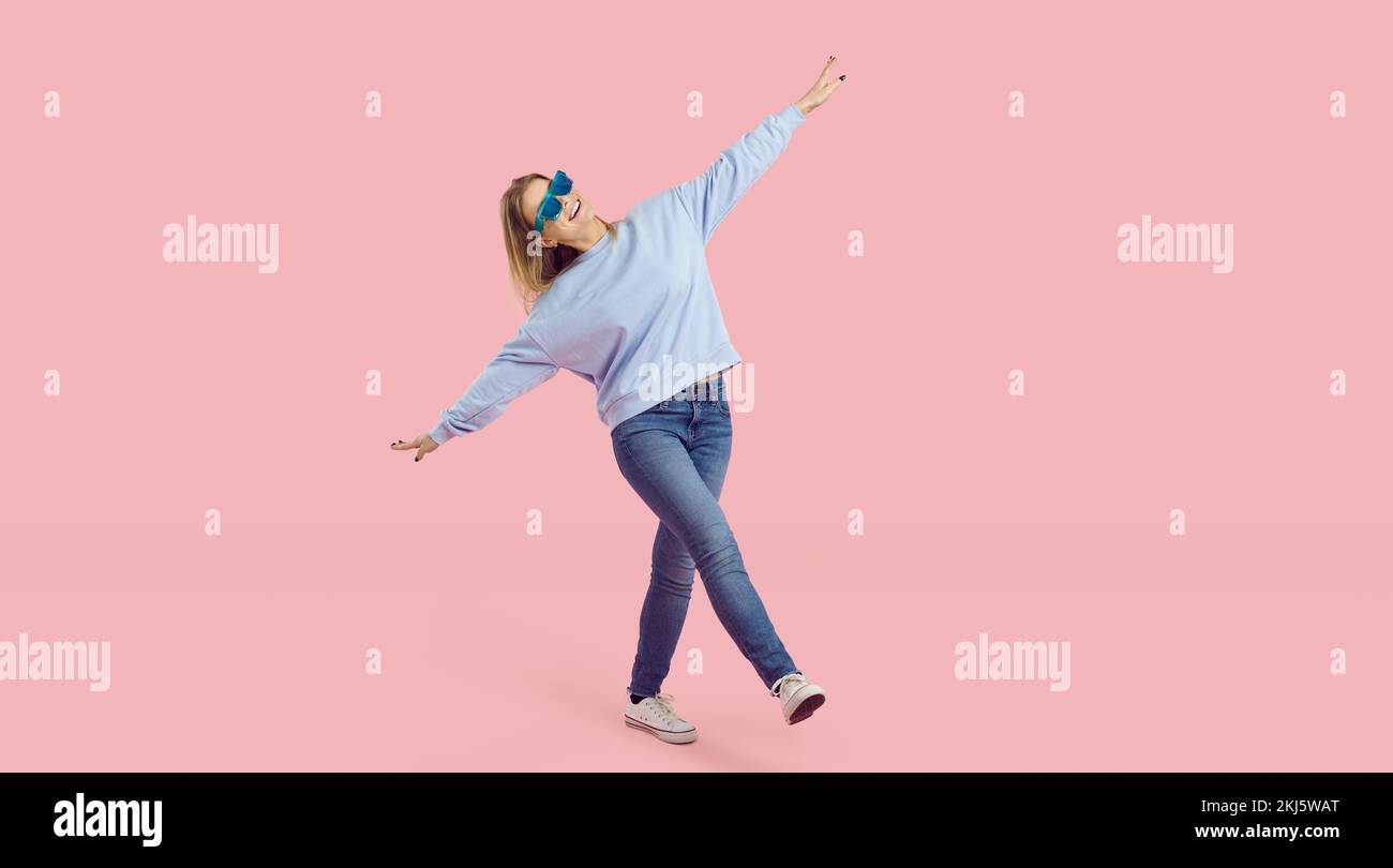 Full body shot of a funny young girl in a casual outfit and sunglasses having fun in the studio Stock Photo