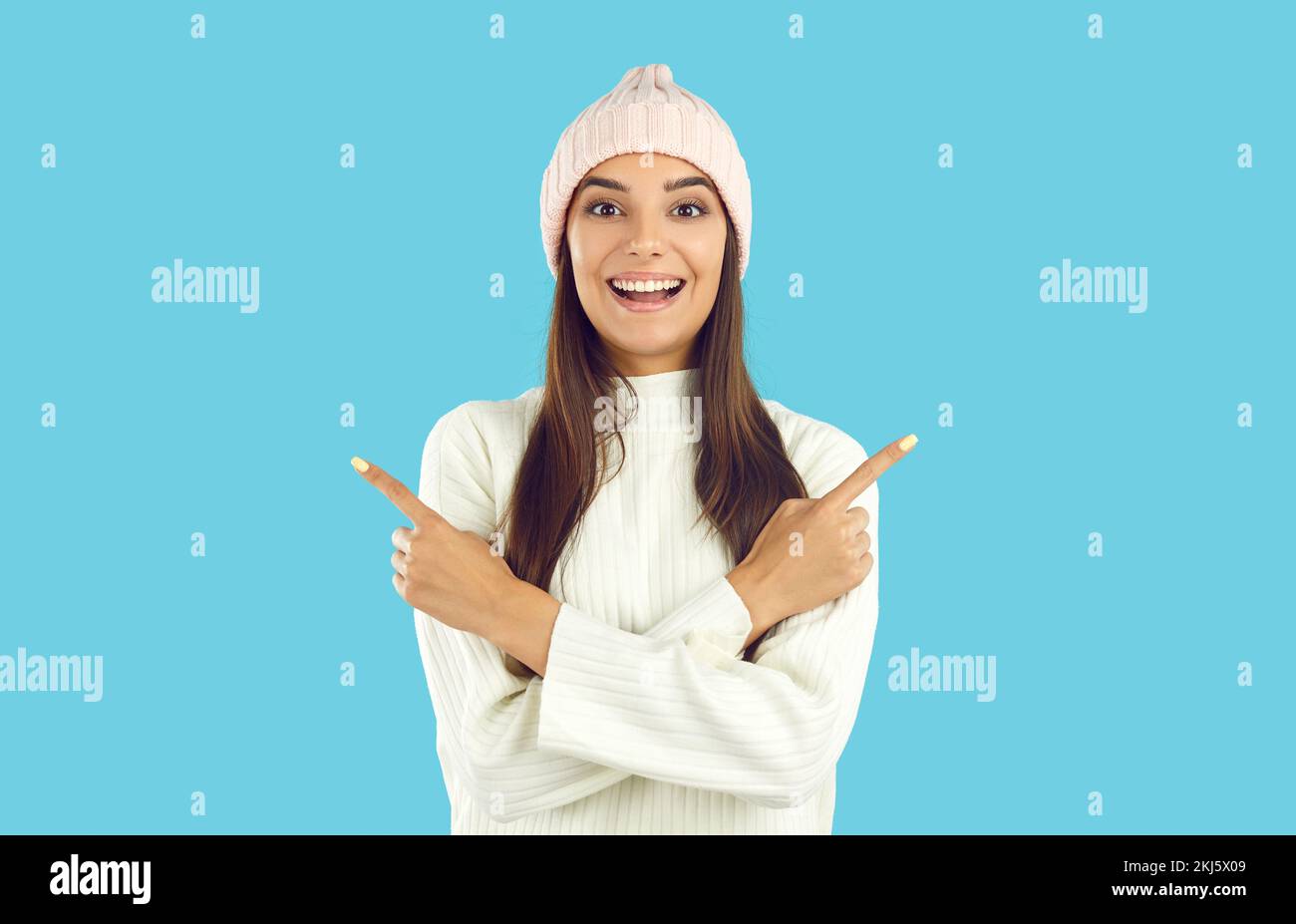 Happy woman in winter hat and sweater points at copy space on two sides of blue background Stock Photo
