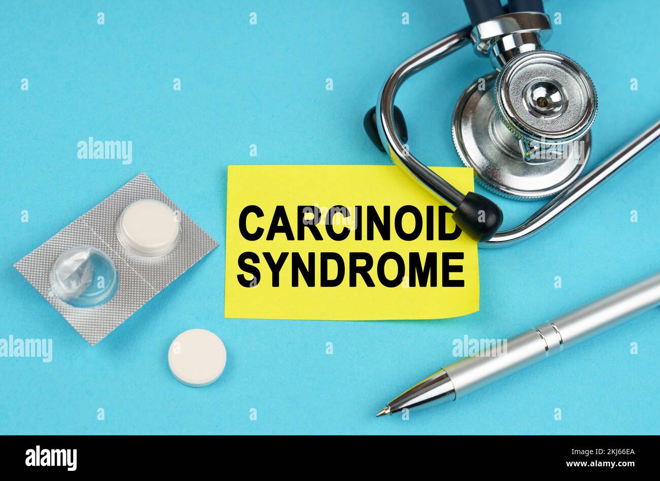 Medical concept. On a blue surface, a stethoscope, pills, a pen and a yellow sticker with the inscription - Carcinoid syndrome Stock Photo