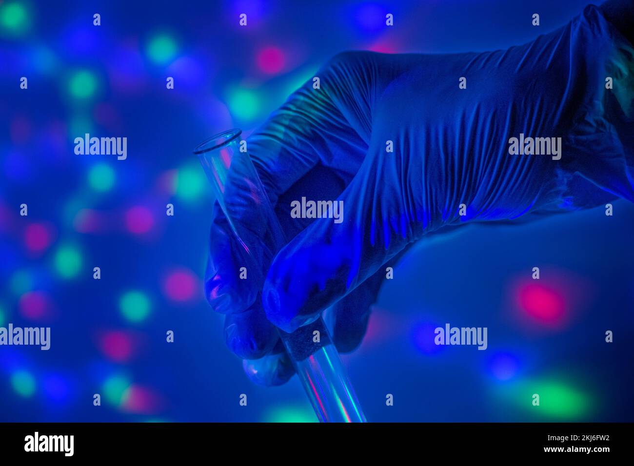 Laboratory test tube in the hand of a doctor in a blue glove against the background of multi-colored bokeh in the evening. Test immunization and Stock Photo