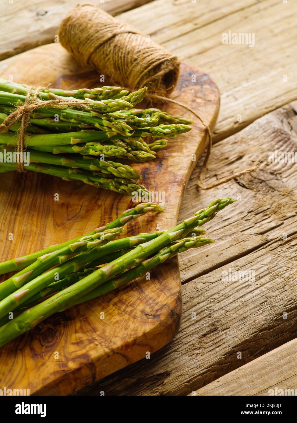 Lots of fresh asparagus on a cutting board. Nearby lies a skein of twine on a simple wooden