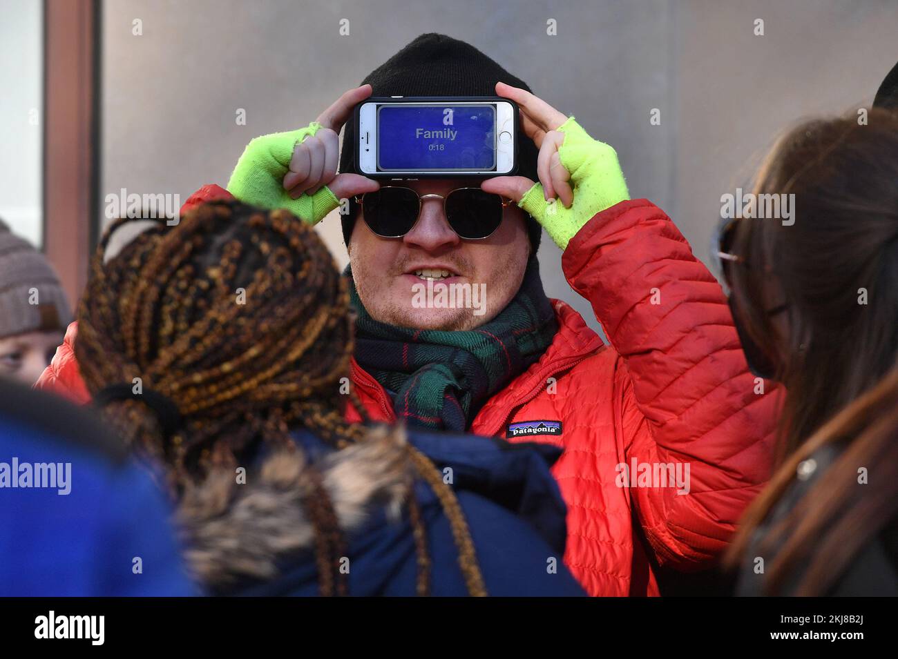 New York, USA. 24th Nov, 2022. A man plays the game Heads Up on his cell phone with family along Central Park West while waiting for the start of the 96th Annual Macy's Thanksgiving Day Parade in New York, NY, November 24, 2022. (Photo by Anthony Behar/Sipa USA) Credit: Sipa USA/Alamy Live News Stock Photo