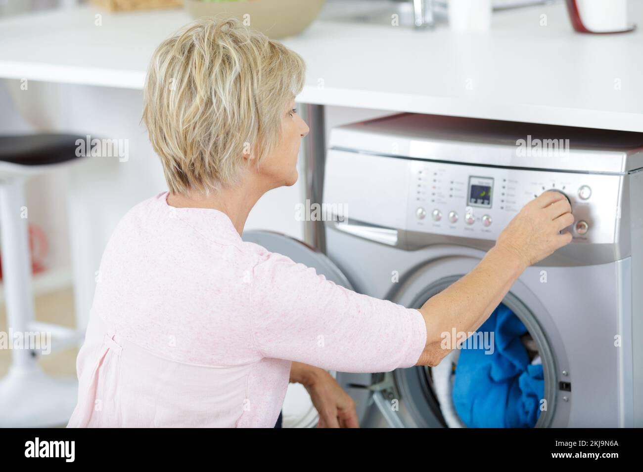 senior woman loading washing machine at home Stock Photo