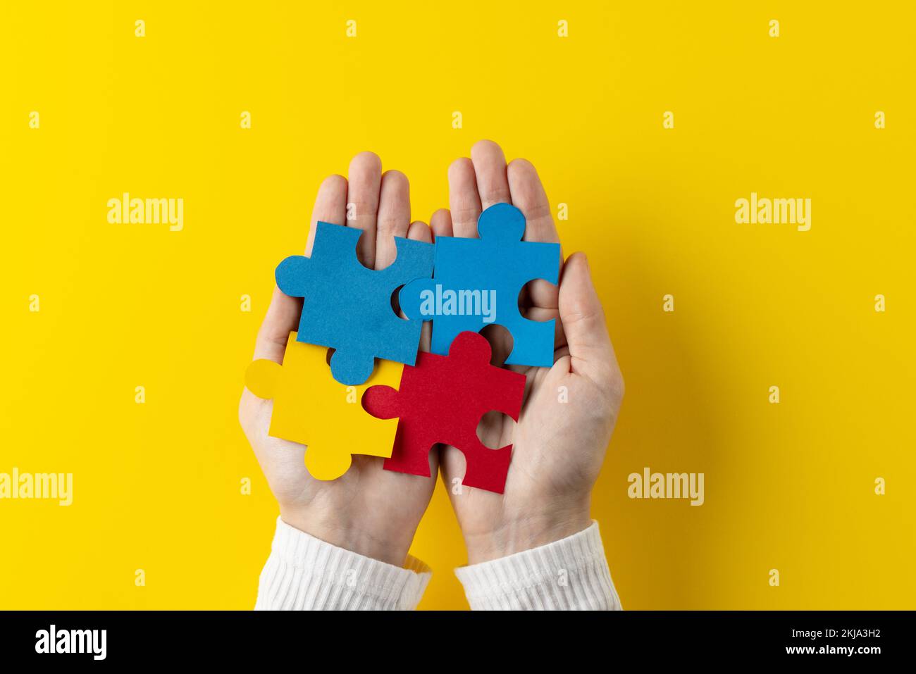 Composition of hands holding jigsaw puzzle pieces on yellow background with copy space Stock Photo