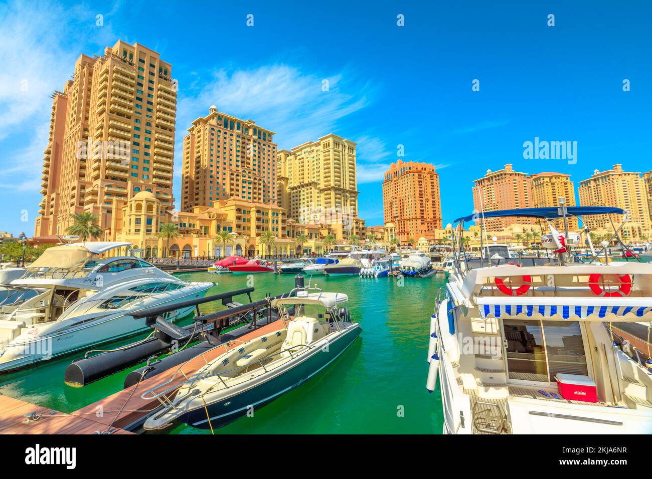 Doha, Qatar - February 18, 2019: Marina corniche promenade in Porto Arabia at the Pearl-Qatar, Doha, with residential towers and luxury boats and Stock Photo