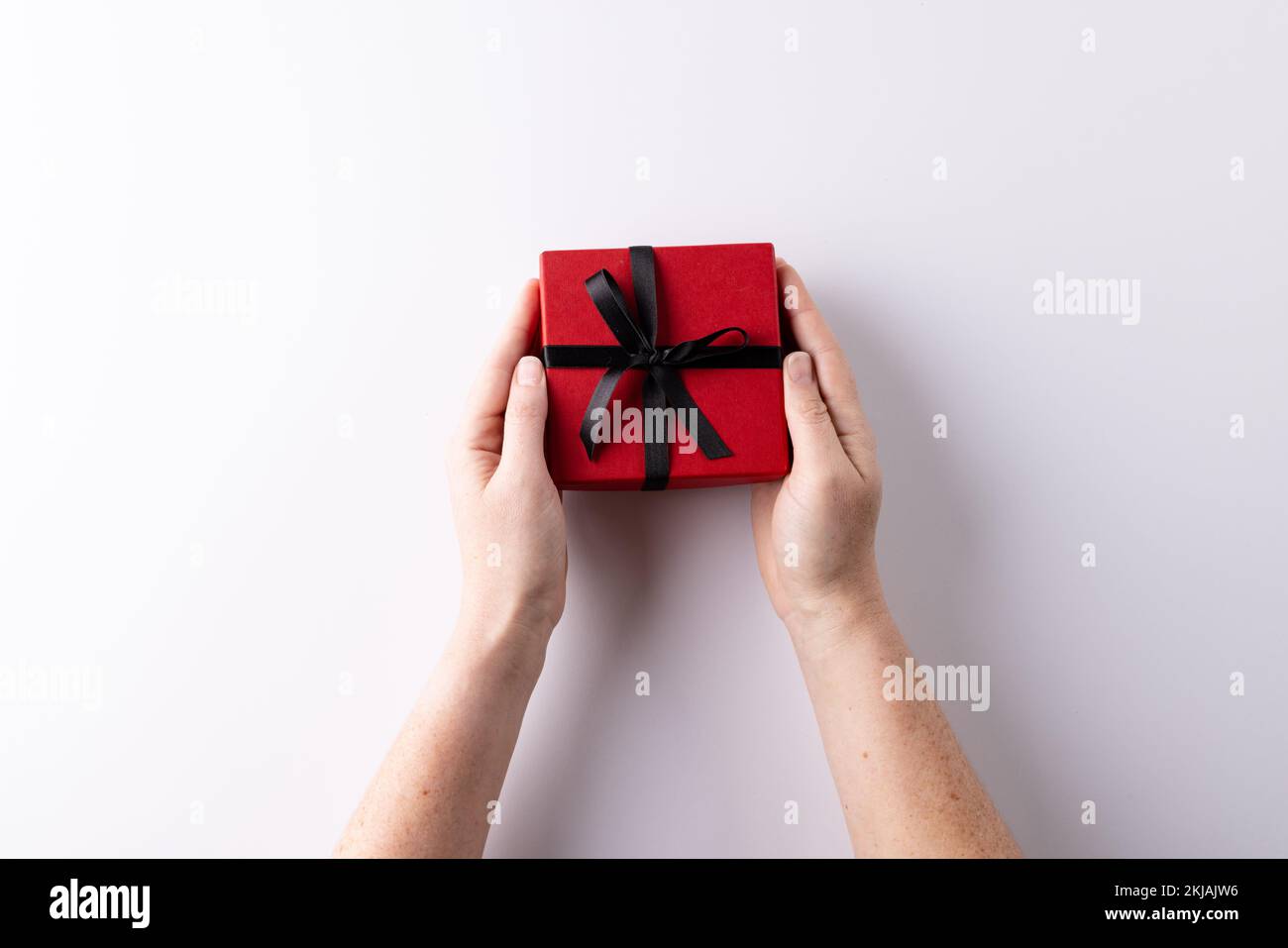 Female hand hold a box wrapped in red paper and tied with a red
