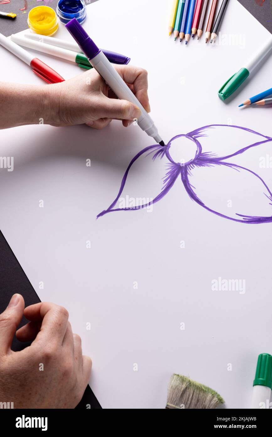 Vertical image of hands drawing purple flower on paper and art materials on table top, copy space Stock Photo