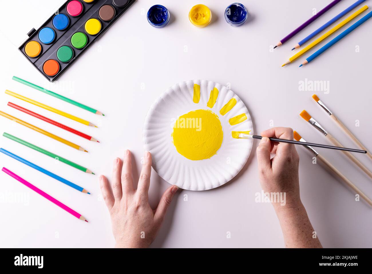 https://c8.alamy.com/comp/2KJAJWE/overhead-of-hands-painting-with-yellow-paint-on-paper-plate-with-art-materials-on-table-top-2KJAJWE.jpg