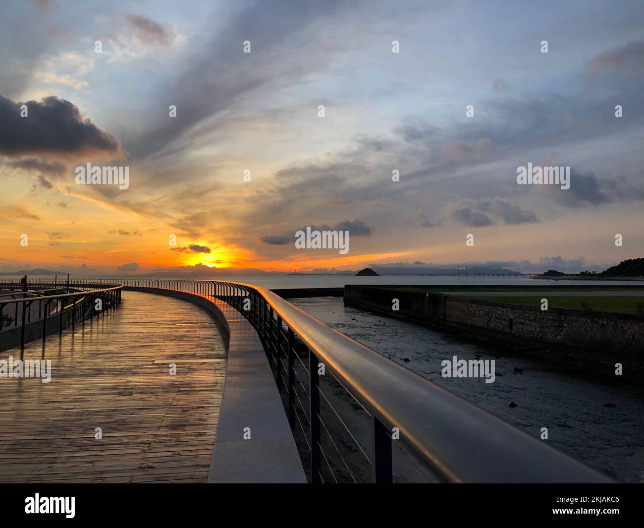 A coastal landscape with a pier under a cloudy sunset sky Stock Photo ...