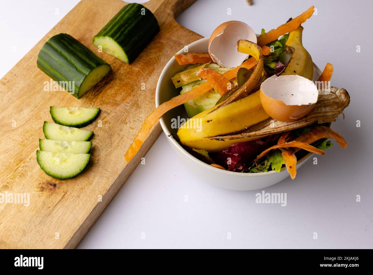 Cucumber on chopping board with organic food waste in kitchen composting bin Stock Photo