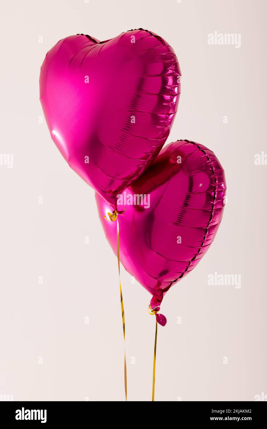 Vertical of two shiny pink heart shaped balloons floating on white ...