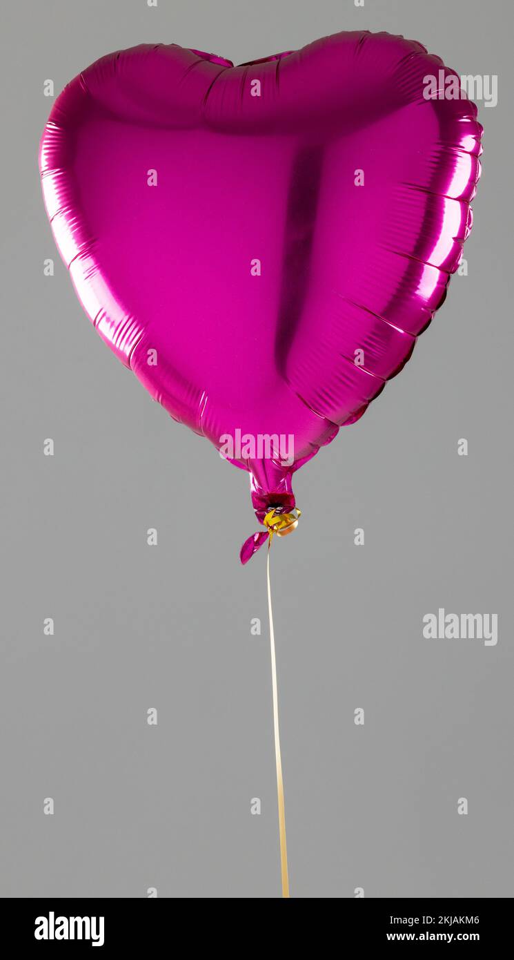 Vertical of shiny pink heart shaped balloon floating on grey background ...