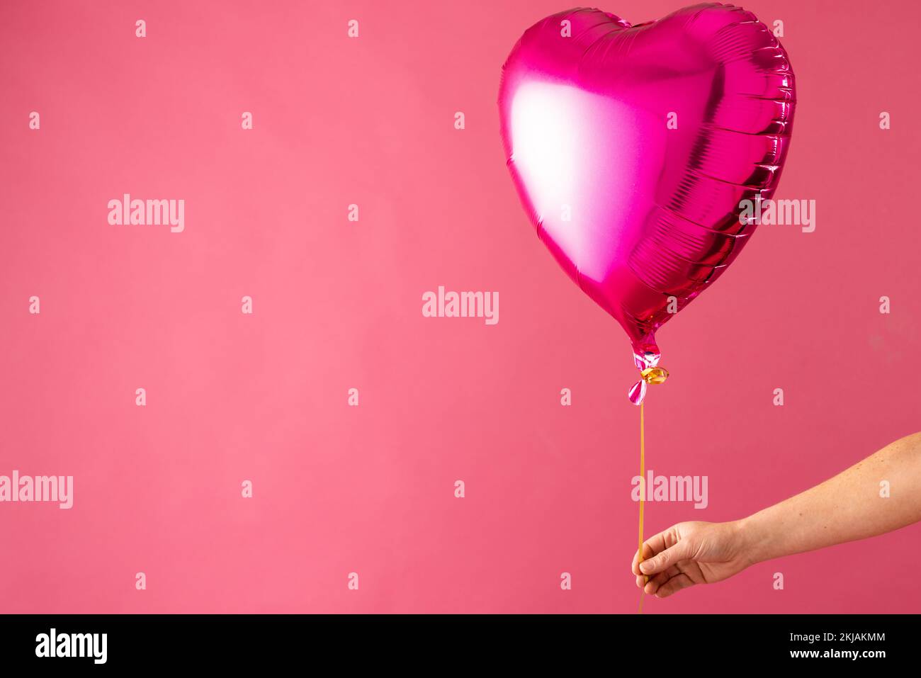 Hand holding shiny pink heart shaped balloon floating on pink ...