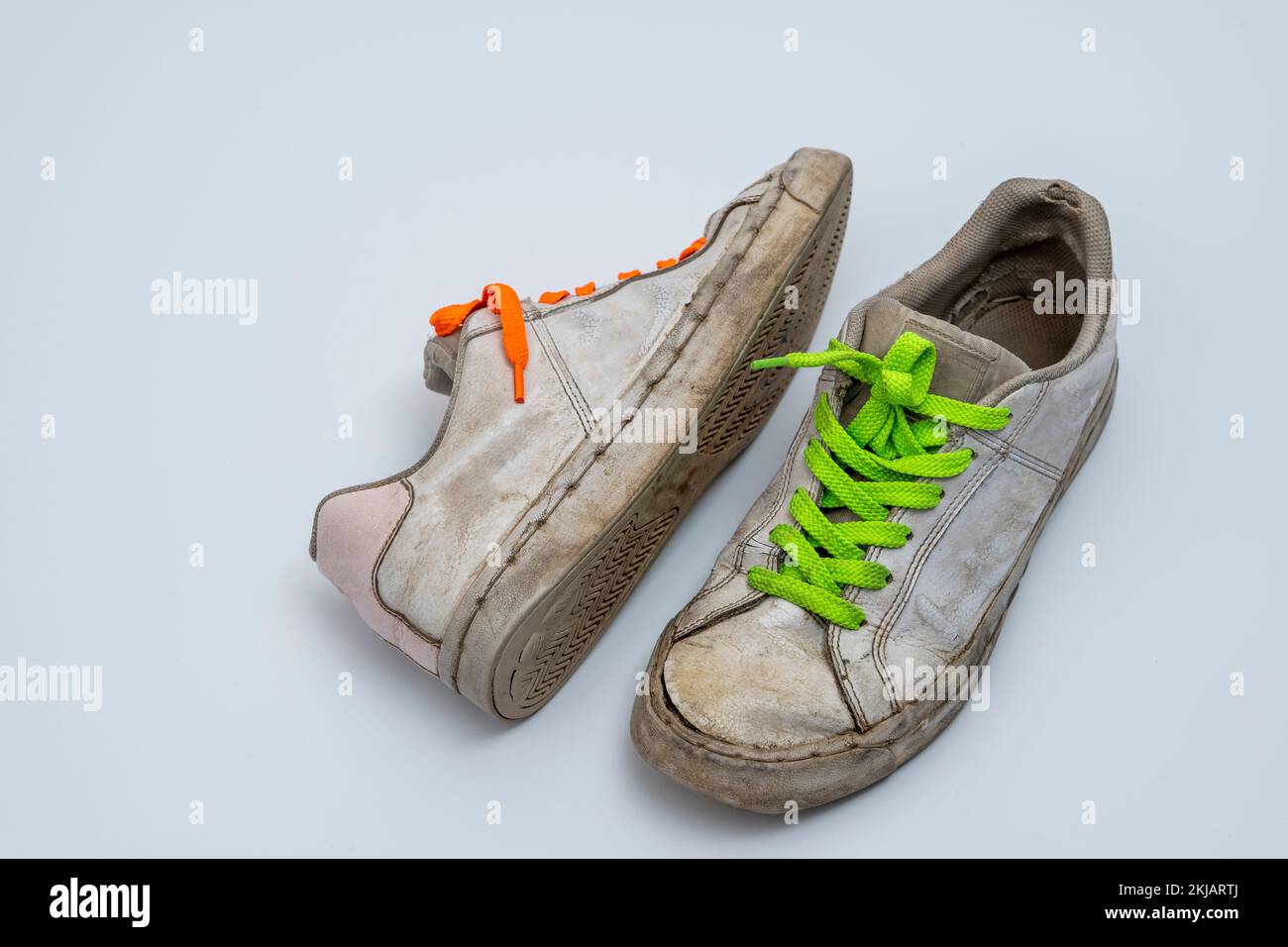 worn old torn white sneakers with colored laces on a white background ...