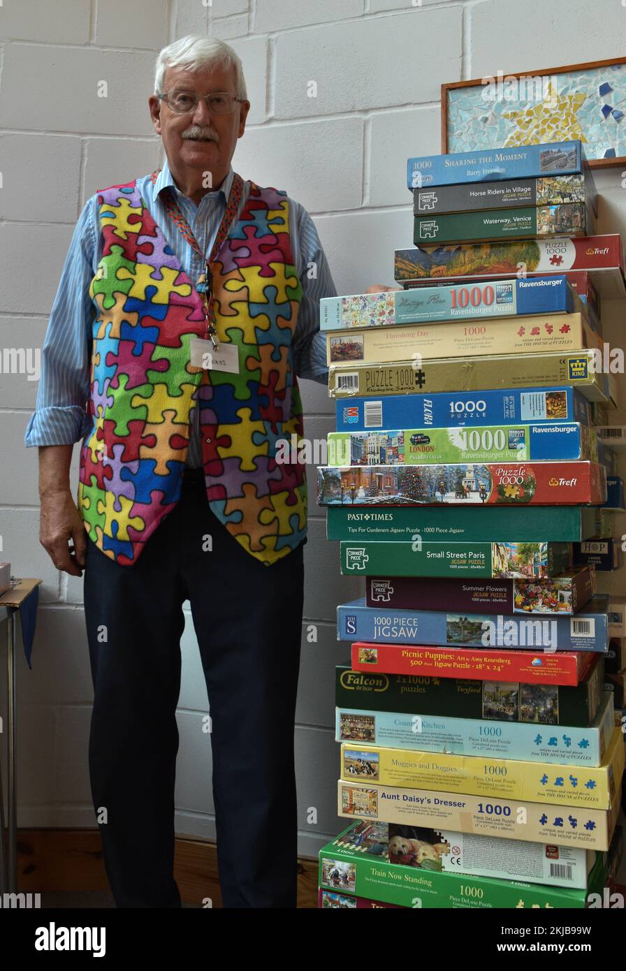 A Volunteer Standing Next To A Stack Of Puzzle Boxes With The Complete