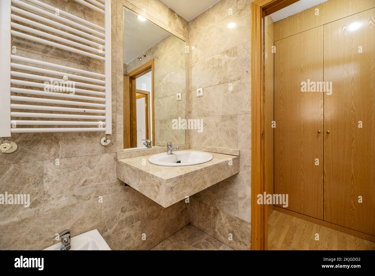 En-suite bathroom with marble countertops, inlaid wall mirror and white heated towel rail and hallway cabinets Stock Photo