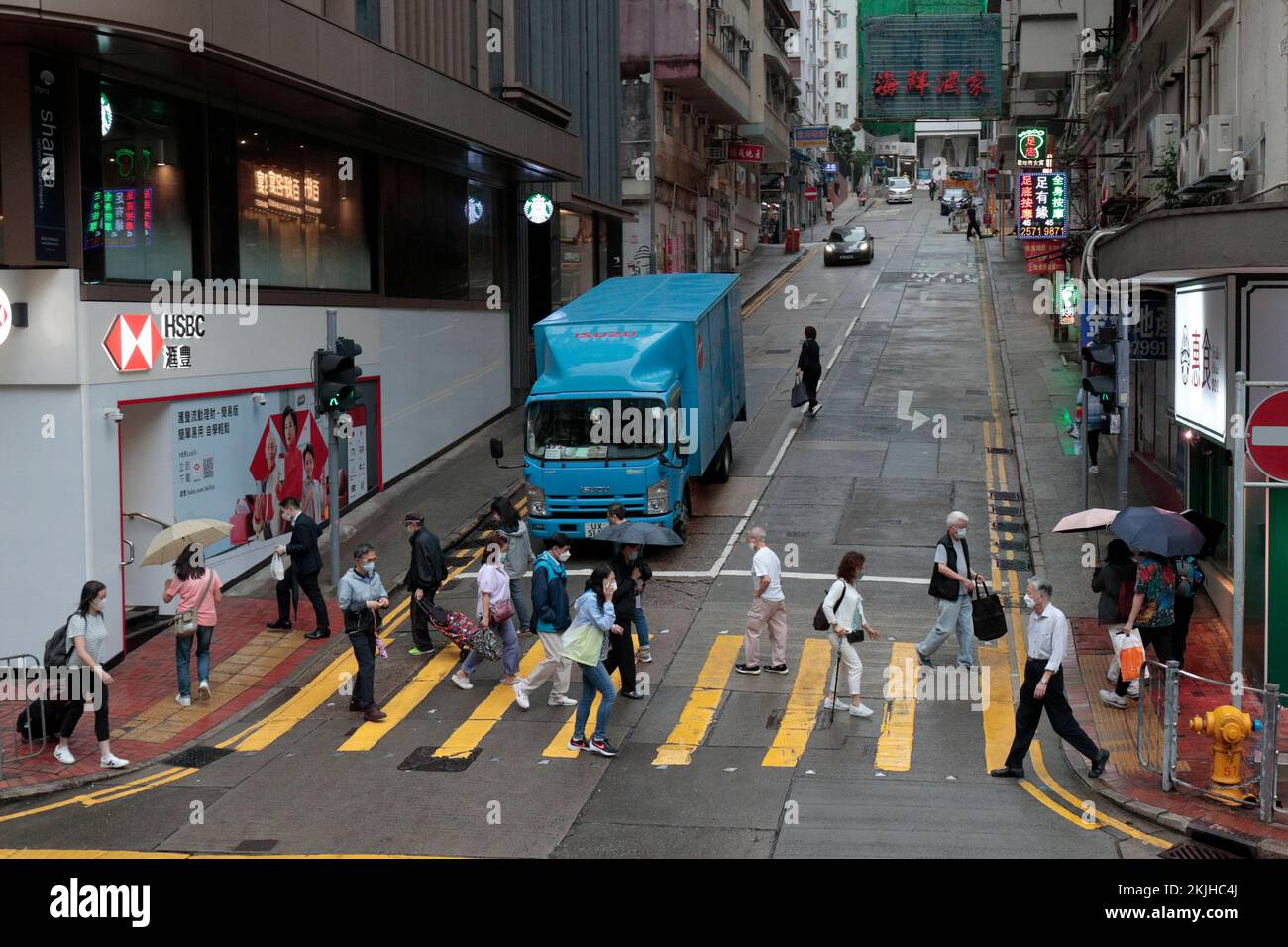 Pedestrians crossing Cheung Hong Street at junction of Kings Road, North Point, in light rain, Hong Kong 24 Nov 2022 Stock Photo