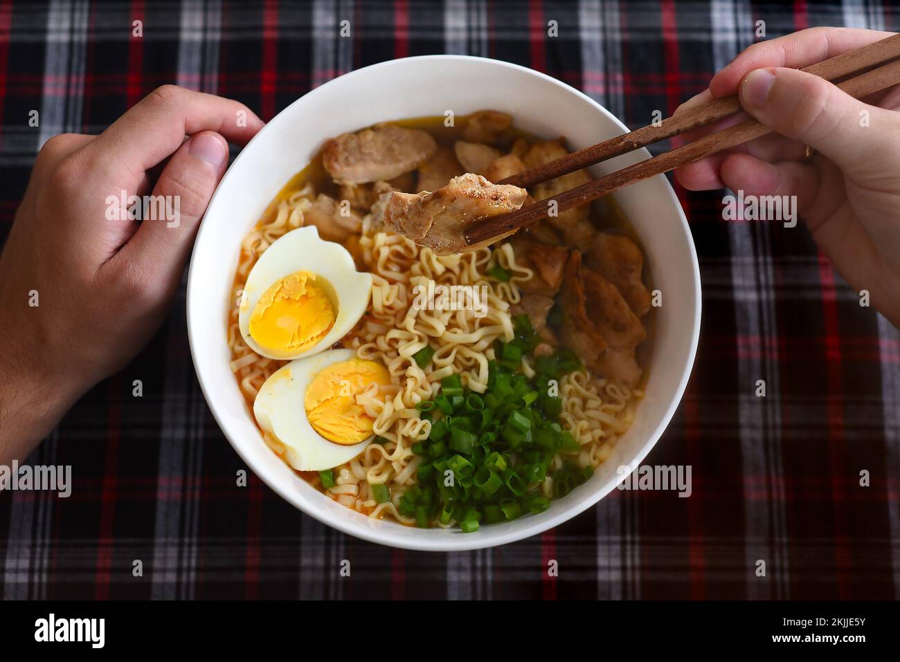 Piece of chicken in chopsticks with japanese ramen and males hands Stock Photo