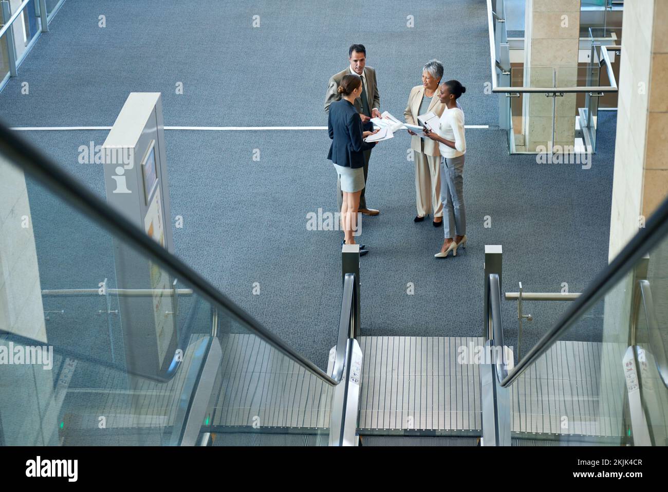 Theres no elevator to success, you have to take the stairs. businesspeople talking at the foot of an escalator. Stock Photo