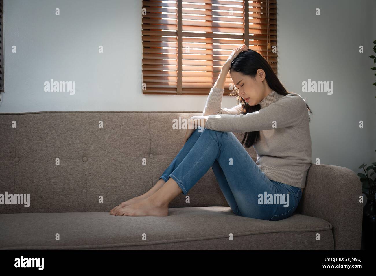 Young lonely attractive asian woman crying on couch feeling sad tired and worried suffering depression isolated at home. Mental Health and lockdown Stock Photo