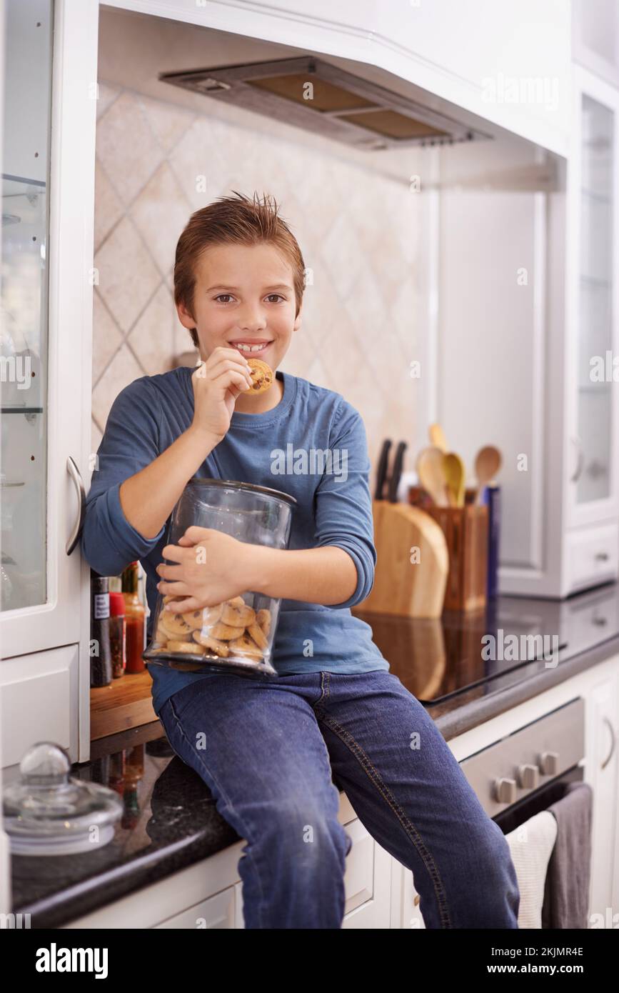 Hands in the cookie jar. A young boy eating a cookie while holding a cookie jar. Stock Photo