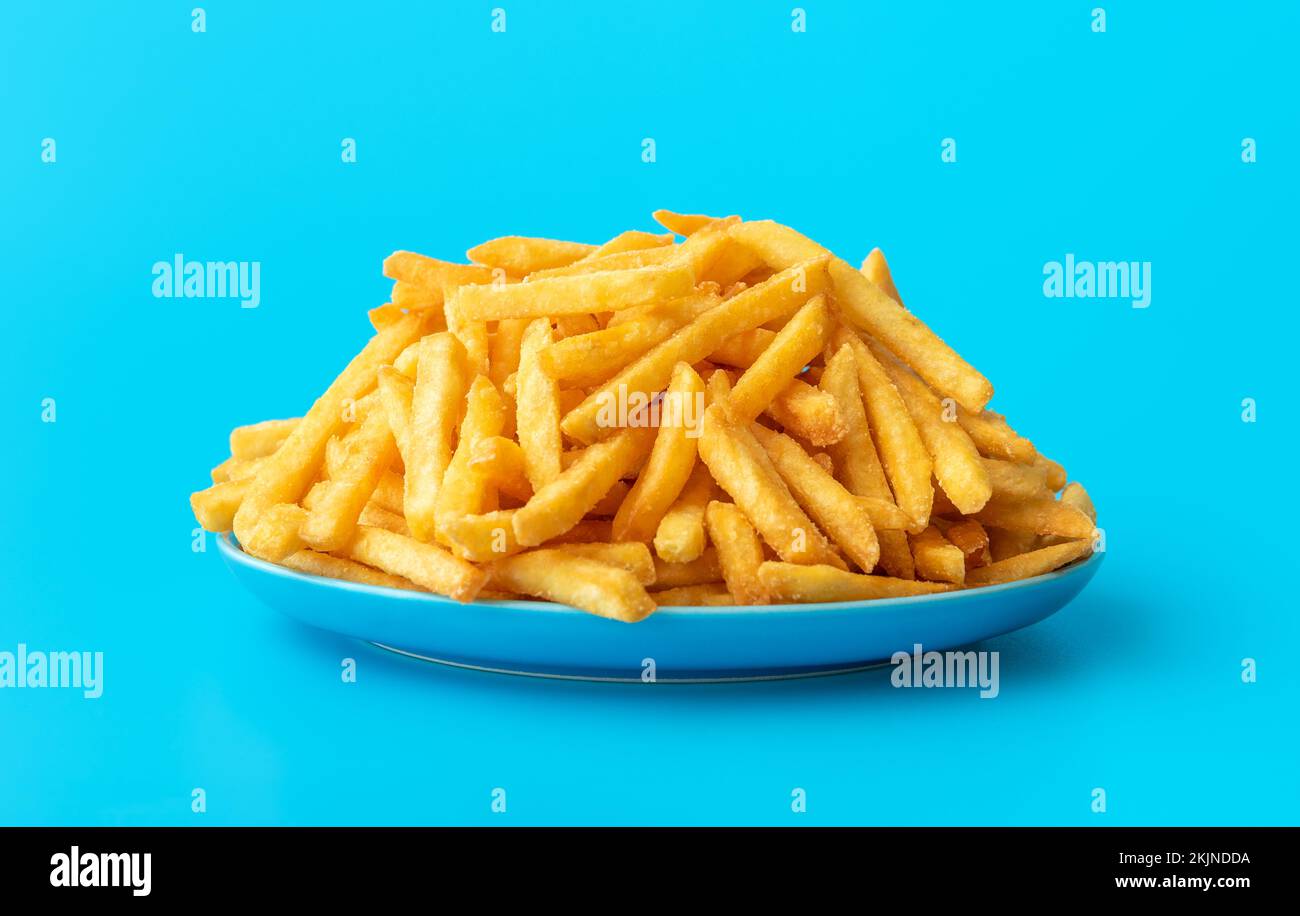 Plate with homemade french fries, minimalist on a blue table. Close-up with delicious fried potatoes on a plate. Stock Photo