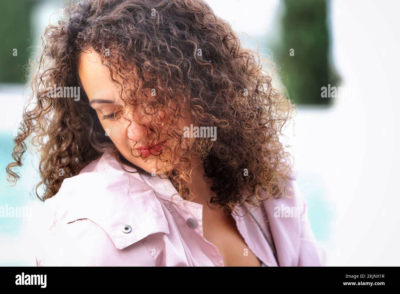 A beautiful Hispanic woman with painted lips and curly hair looking down Stock Photo