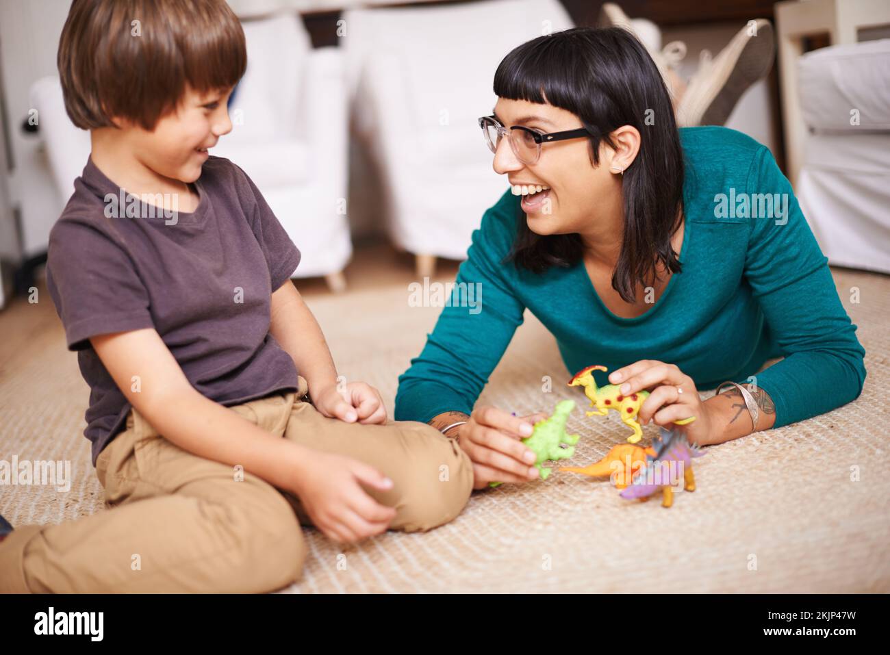 He loves playing dinosaurs with mom. a mother and her son playing with toy dinosaurs. Stock Photo