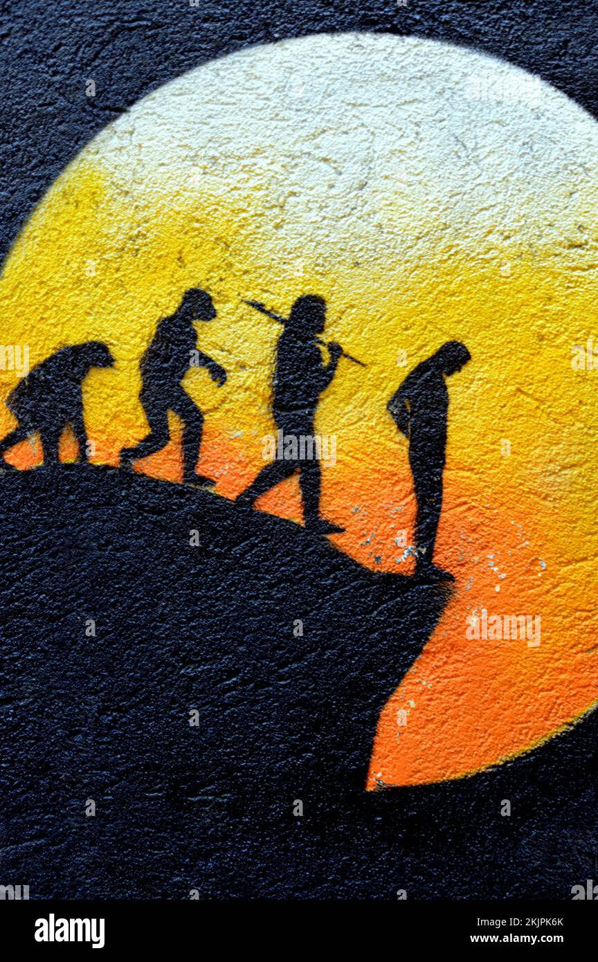 A vertical view of the evolution of man in dark silhouette standing at the edge of a cliff with a large bright sun Stock Photo